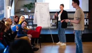 Workshop JSNS – interaktivní školení pro učitele, přednášející stojí u flipchartu a diskutuje s účastníky (učiteli).